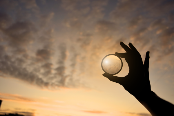 Silhouette of hand holding a round lens, evening light, cloudy sky, sunset colors, concept of vision