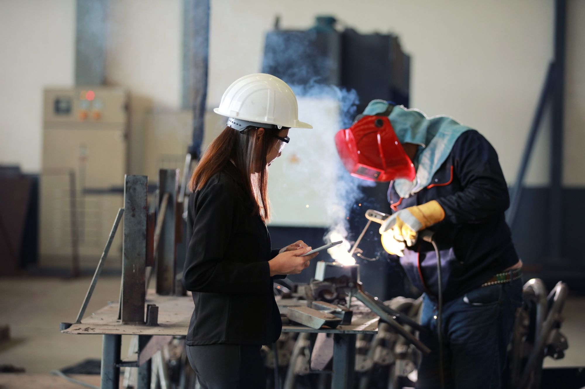 A woman with a tablet auditing a welding man