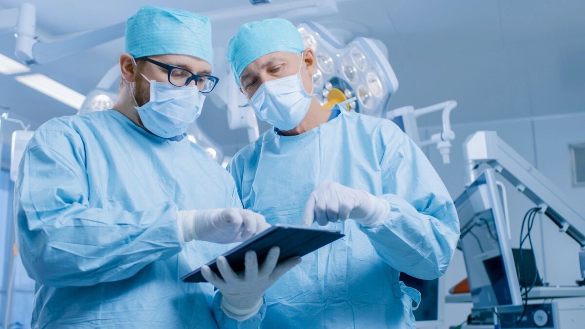 Two Professional Surgeons Use Digital Tablet Computer while Standing in the Modern Hospital Operatin