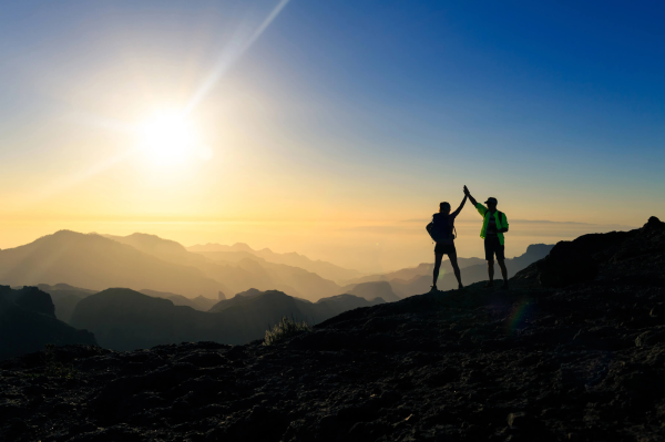 Mountaineers celebrate their ascent to the summit at sunset by clapping their hands.